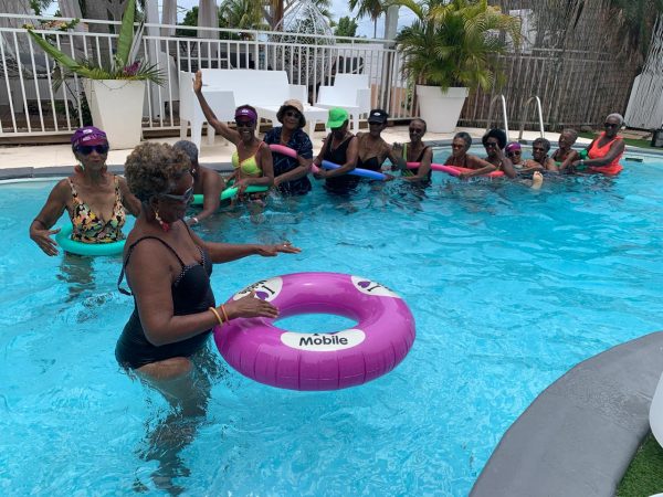 Groupe de femmes âgées faisant un atelier aquatique avec des frites et des bouées colorées dans une piscine.