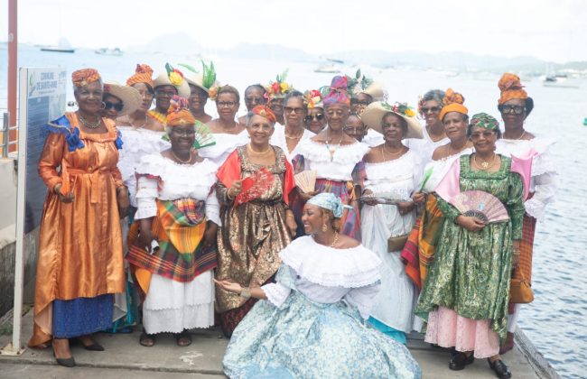 Groupe de femmes âgées en habits traditionnels créoles, souriantes, posant sur un ponton au bord de la mer.