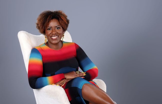 Martine JOACHAS directrice d'Auditec Formation, confortablement installée sur un fauteuil blanc, souriante vêtue d'une robe colorée