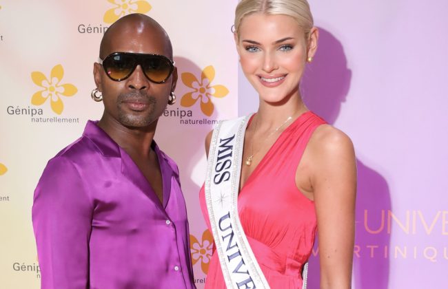 Steeven Jean-Yves Zamor, directeur national de Miss Univers Martinique, vêtu d'un ensemble de soie violet souriant avec à ses côté Victoria Kjaer Theilvig, Miss Univers 2024, souriante avec sa bannière et vêtue d'une robe fuchsia. Une photo de Ludovic LISEE prise devant un photocall du centre commercial Génipa en Martinique.