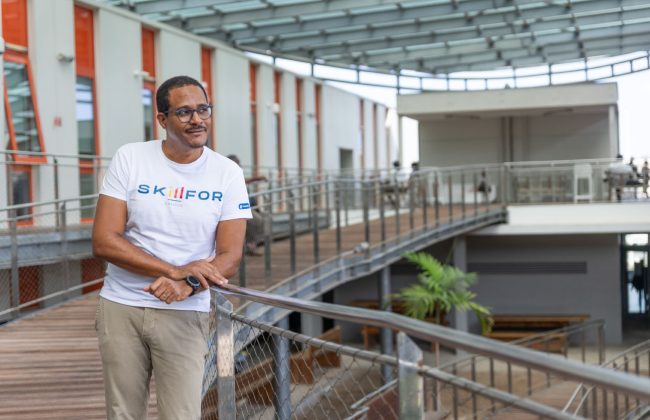 Frédérique Gaval, directeur des programmes et des affaires académiques de Skillfor campus, appuyé contre une rambarde, souriant, dans le campus avec un t-shirt à l'éfigie de l'école