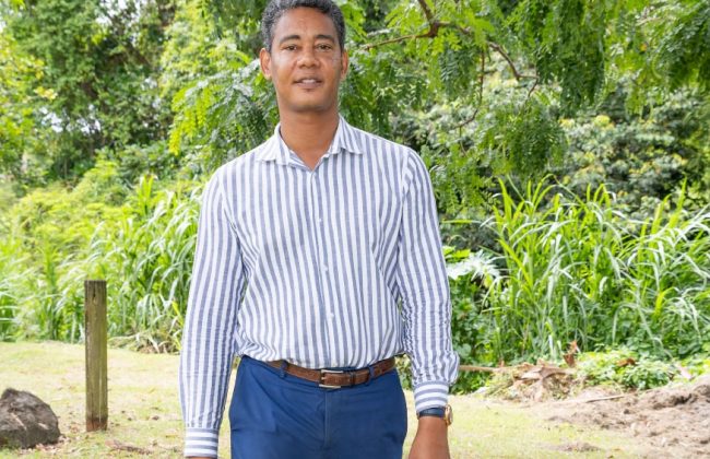 Fred-Michel Tirault, maire du Saint-Esprit, en chemise rayé et pantalon bleu, marchant d'un pas déterminé dans un paysage naturel