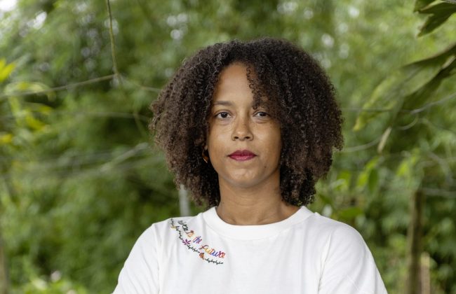Orianne Telle debout souriante bras croisé, en jean et t-shirt blanc dans un environnement nature